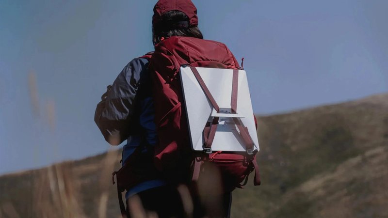 Hiker seen from behind with a Starlink dish strapped to a red backpack